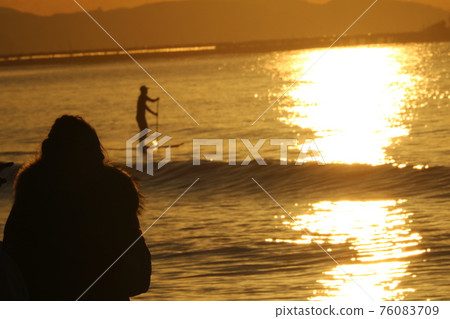 A woman staring at the rising sun and the waves A woman staring at the rising sun and the waves 76083709
