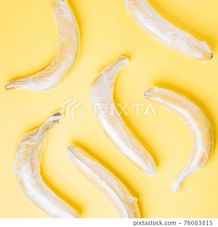 Banana fruits wrapped in stretch plastic on yellow background Banana fruits wrapped in stretch plastic on yellow background 76083815