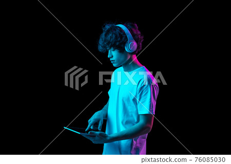 Portrait of young man using tablet isolated over dark background in neon light 76085030