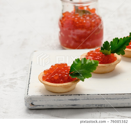 red caviar in a glass jar and round tartlets on a white table red caviar in a glass jar and round tartlets on a white table 76085382