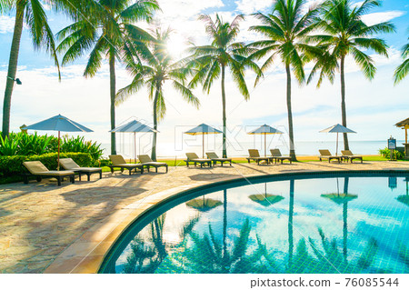 Beautiful luxury umbrella and chair around outdoor swimming pool in hotel and resort with coconut palm tree on blue sky Beautiful luxury umbrella and chair around outdoor swimming pool in hotel and resort with coconut palm tree on blue sky 76085544