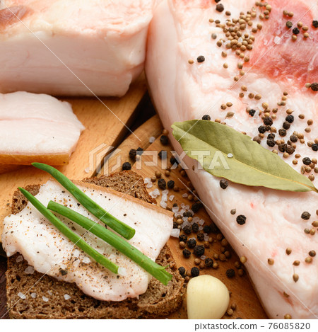 raw pork meat and lard with salt, spices and garlic on a cutting board, dark wooden background raw pork meat and lard with salt, spices and garlic on a cutting board, dark wooden background 76085820
