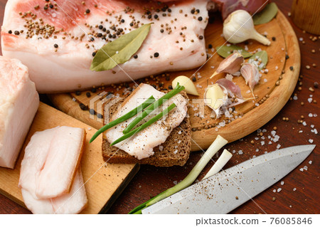 raw pork meat and lard with salt, spices and garlic on a cutting board, dark wooden background 76085846