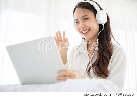 Happy beautiful young asian woman working on computer laptop and sitting on bed in house 76086130