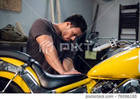 A modern young man in a t-shirt and jeans is engaged in bike diagnostics in a repair shop or garage. 76086180