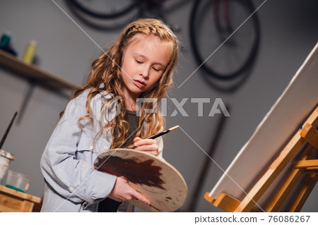 An art school student mixes colors on a palette for her canvas drawing in a workshop. 76086267