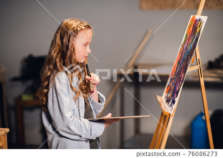 Young girl creative artist at work in a workshop. With passion draws a picture immersed in work. 76086273