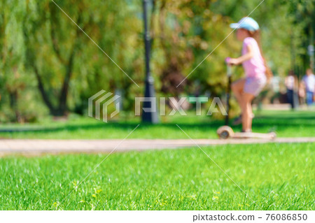 a child girl rides a scooter in a city park, summer day, green lawn with grass and trees, bright sunlight and shadows a child girl rides a scooter in a city park, summer day, green lawn with grass and trees, bright sunlight and shadows 76086850