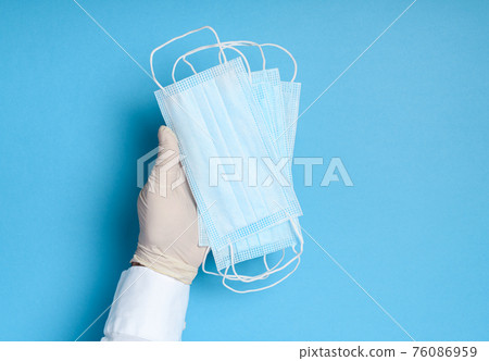 hands in medical gloves with a medical breathing mask on a blue background, health care prevention of coronavirus infection, as well as other viruses and pollution hands in medical gloves with a medical breathing mask on a blue background, health care prevention of coronavirus infection, as well as other viruses and pollution 76086959