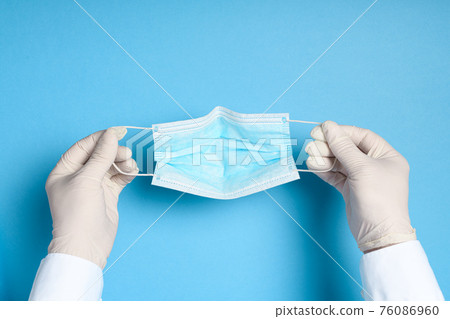 hands in medical gloves with a medical breathing mask on a blue background, health care prevention of coronavirus infection, as well as other viruses and pollution hands in medical gloves with a medical breathing mask on a blue background, health care prevention of coronavirus infection, as well as other viruses and pollution 76086960