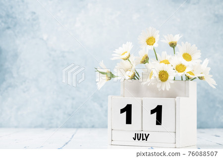 cube calendar for July with daisy flowers over blue 76088507
