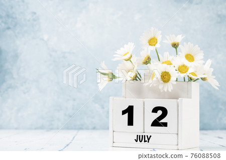 cube calendar for July with daisy flowers over blue 76088508