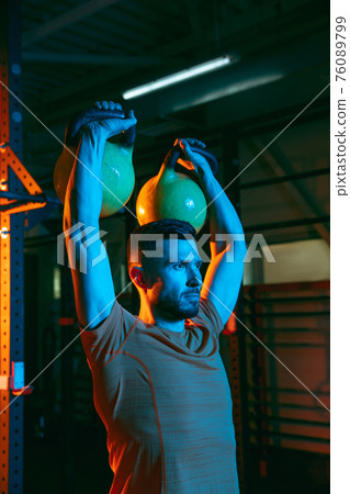 Young athletic man, fitness instructor training in gym in mixed neon light. Young athletic man, fitness instructor training in gym in mixed neon light. 76089799