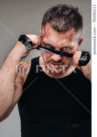 on a gray background stands a battered man in a black T shirt looking like a fighter and preparing for a fight 76090213