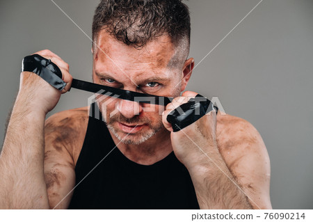 on a gray background stands a battered man in a black T shirt looking like a fighter and preparing for a fight 76090214