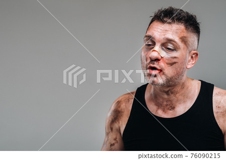 a battered man in a black T shirt who looks like a drug addict and a drunk stands against a gray background a battered man in a black T shirt who looks like a drug addict and a drunk stands against a gray background 76090215