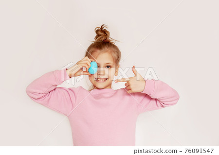Cute happy girl holding an Easter egg in her hands. Portrait of a child on a light background with space for text Cute happy girl holding an Easter egg in her hands. Portrait of a child on a light background with space for text 76091547