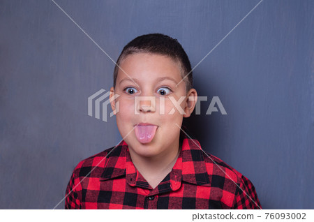 White teenage boy with light brown hair, wearing a red plaid shirt, grimaces and sticks out his tongue on isolated gray background White teenage boy with light brown hair, wearing a red plaid shirt, grimaces and sticks out his tongue on isolated gray background 76093002