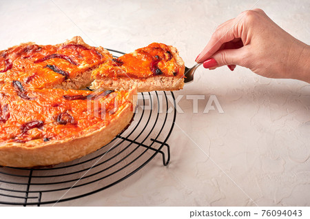 Woman's hand holds on a shoulder blade piece of homemade quiche  76094043