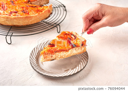 Woman's hand holds on a shoulder blade piece of homemade quiche  76094044