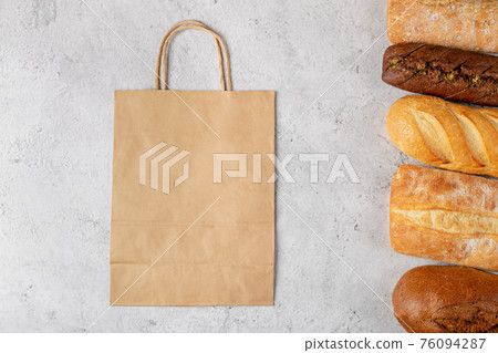 Baking background with eco disposable paper bag from a supermarket recyclable and whole fresh baked loaves of bread top view on gray background with mockup 76094287