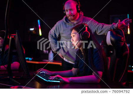Esports team training camp in computer club with coach, caucasian guy and asian girl 76094792