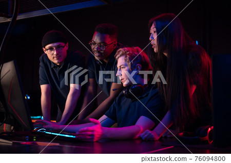 Two guys and a girl in medical masks in a computer club give support to their friend during his game 76094800