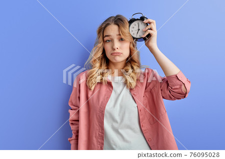 Sleepy woman with alarm clock attached to head 76095028