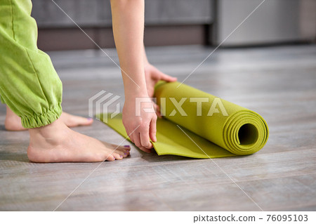 cropped woman folding green yoga or fitness mat after working out at home in living room 76095103