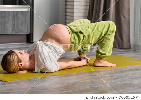 flexible pregnant woman lifting body up while lying on floor on fitness mat flexible pregnant woman lifting body up while lying on floor on fitness mat 76095157