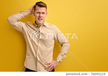 doubtful young caucasian guy stand thinking, scratch back of head 76095229