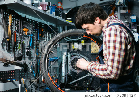 Bicycle mechanic fixing cycle wheel in repair shop. Velocipede service. Repairer male bike shop engineer fix bicycle wheel in workshop. Technician fixes bike parts. Handyman at work in the workplace 76097427