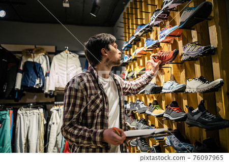Sales assistant sports travel store makes inventory hiking boots. Travel goods store theme. Clothes and footwear for sports and travel. Store manager near shelves with hiking boots makes check list Sales assistant sports travel store makes inventory hiking boots. Travel goods store theme. Clothes and footwear for sports and travel. Store manager near shelves with hiking boots makes check list 76097965