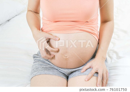 Pregnant woman scratching her belly sitting on bed at home Skin problems and pores in teenagers. Pregnant woman scratching her belly sitting on bed at home Skin problems and pores in teenagers. 76101750