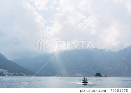 A small tourist boat sails on the Bay of Kotor with the islands in the background near Perast in Montenegro, against the backdrop of mountains and clouds in the sky. A small tourist boat sails on the Bay of Kotor with the islands in the background near Perast in Montenegro, against the backdrop of mountains and clouds in the sky. 76101978