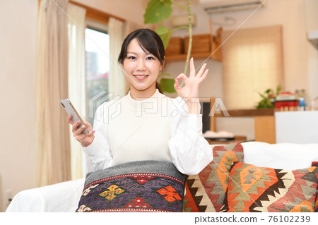 A young woman holding a smartphone and signing OK A young woman holding a smartphone and signing OK 76102239