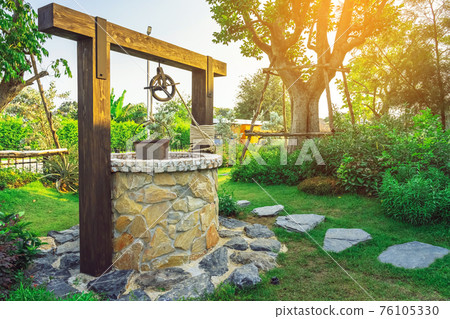 Beautiful artesian well made by stones and wheel pulley with metal bucket and rope in peaceful garden atmosphere. Retro stone water well in rural area. Garden decoration with antique items. Beautiful artesian well made by stones and wheel pulley with metal bucket and rope in peaceful garden atmosphere. Retro stone water well in rural area. Garden decoration with antique items. 76105330