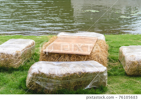 Seats and tables made from straw bales for event and party laid on lawn yard. Straws stubble decorated for sitting in the countryside. Furniture made of pallets and straw bales. Selective focus. 76105683
