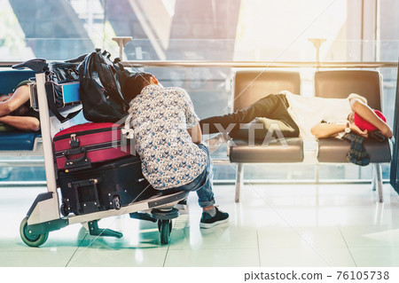 Tired passenger napping on a trolley while waiting for boarding in the in airport terminal. 76105738