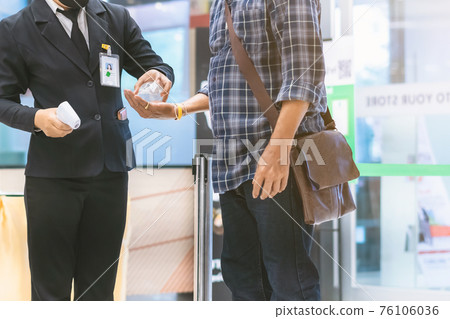 Hand of customer waits for a drop of alcohol gel from female security guard to prevent the spread of germs and bacteria and avoid infections Corona virus (Covid-19) before entering the mall. 76106036