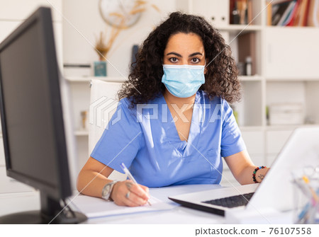 Doctor in mask working on laptop 76107558