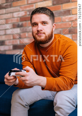 Close-up view of bearded handsome bearded young man holding controllers and playing video games on console Close-up view of bearded handsome bearded young man holding controllers and playing video games on console 76107647
