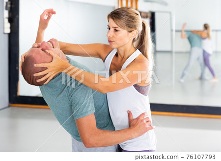 Sporty woman with a trainer conducts painful reception on the eyes in gym Sporty woman with a trainer conducts painful reception on the eyes in gym 76107793