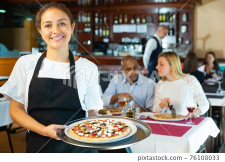 Hospitable latin american waitress meeting guests in pizzeria Hospitable latin american waitress meeting guests in pizzeria 76108033