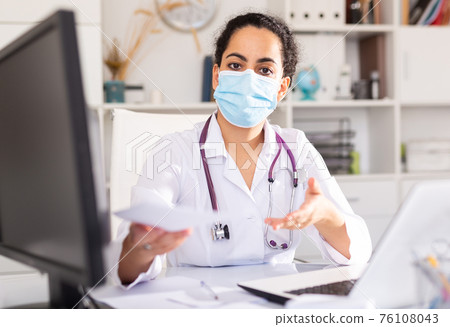 Woman doctor in mask explaining prescription Woman doctor in mask explaining prescription 76108043