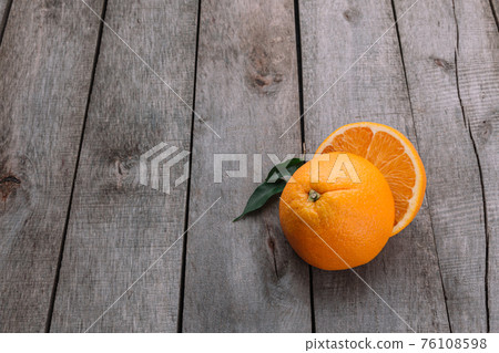 Halves of orange fruit on gray wooden background. Orange pulp and green leaves Halves of orange fruit on gray wooden background. Orange pulp and green leaves 76108598