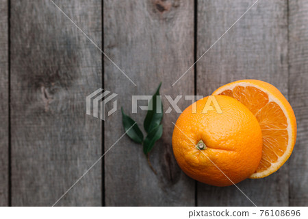 Halves of orange fruit on gray wooden background. Orange pulp and green leaves Halves of orange fruit on gray wooden background. Orange pulp and green leaves 76108696