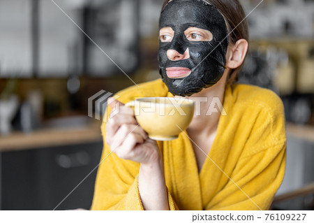 Woman with black cleansing mask on her face on the kitchen at home 76109227
