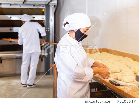 Woman baker dividing raw dough into portions in bakery 76109517
