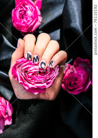 AMOR word on nails manicure hold Pink rose flower on black silk fabric. Minimal flat lay nature. Female hand. Love AMOR word on nails manicure hold Pink rose flower on black silk fabric. Minimal flat lay nature. Female hand. Love 76110192